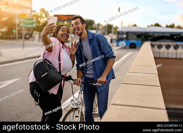 Happy young man with woman taking selfie through mobile phone at footpath
