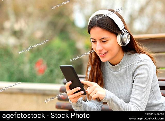 Happy teen using smart phone listening to music with headphones in a park