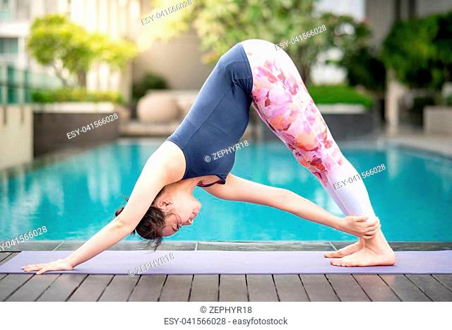 Beautiful young Asian happy woman doing yoga exercise near swimming pool. Healthy lifestyle and good wellness concepts