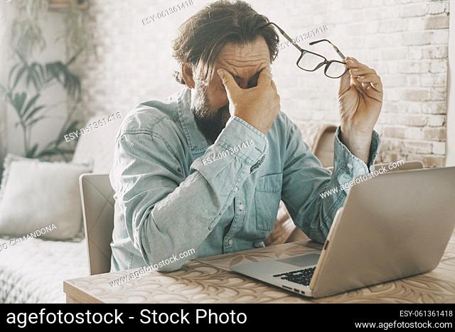 Tired man holding glass and touching is eyes after over work on notebook computer. Online activity and problems to solve concept