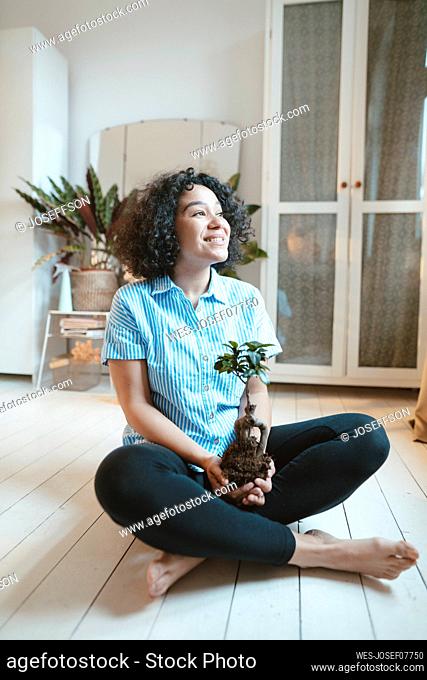Smiling woman sitting with houseplant on floor at home
