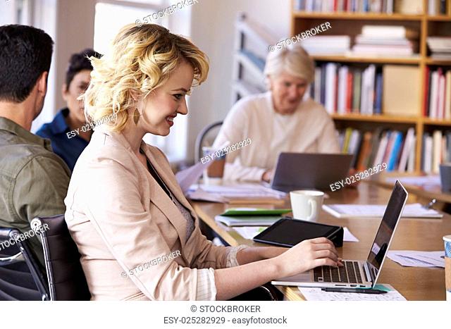 Businesswoman Using Laptop At Desk In Busy Office