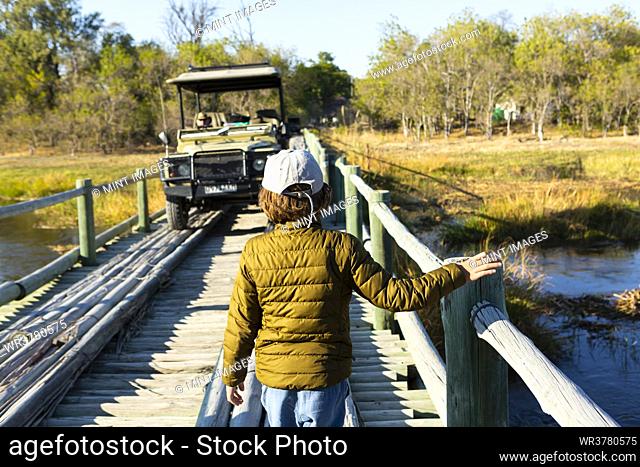 A boy walking across a wooden bridge over marshland