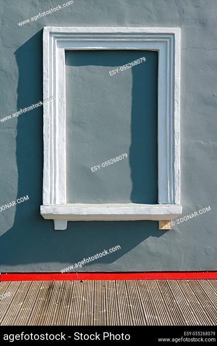 Gray plastered wall and blind imitation window with a white frame. Real sunny day outdoor shot
