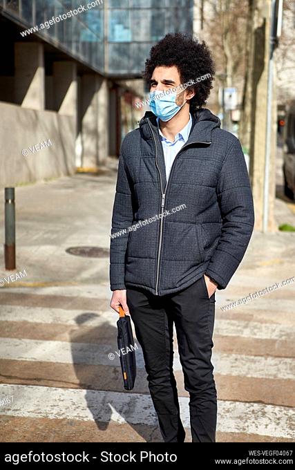 Afro man with laptop bag wearing protective face mask during pandemic