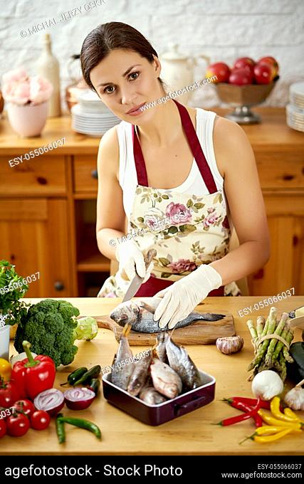 beautiful young woman, brunette prepares fresh fish at a table full of organic vegetables