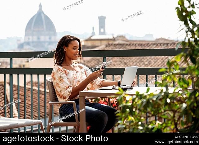 Young woman using laptop and smartphone on a balcony in Florence, Italy