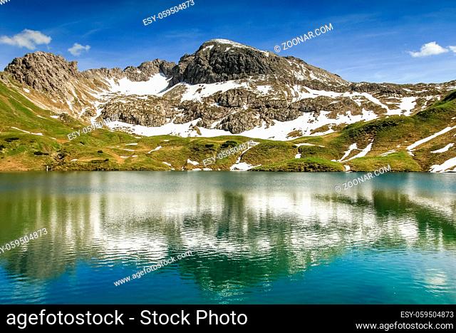 Beautiful reflections in the remote Schrecksee lake up high in the alpine mountains spotted with snow in spring or summer. Bavaria, Allgau, Germany