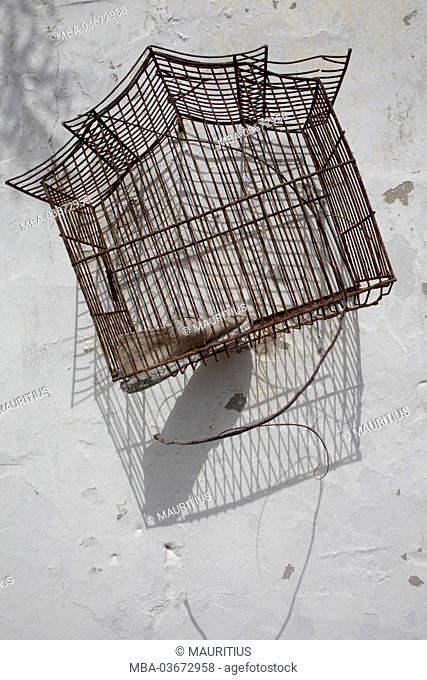 Shoe in a bird cage on exterior wall, shade