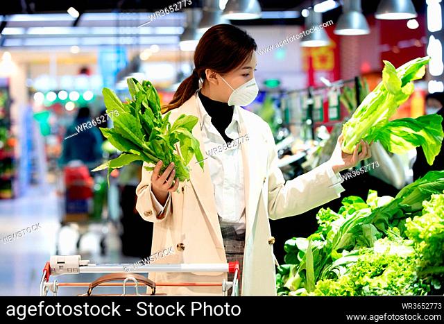 Wearing a mask of the young woman in the supermarket to buy vegetables