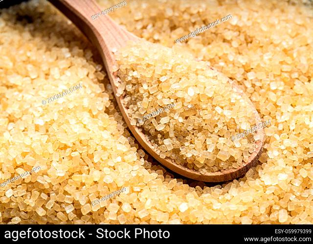 wooden spoon with demerara brown cane sugar close up on pile of sugar