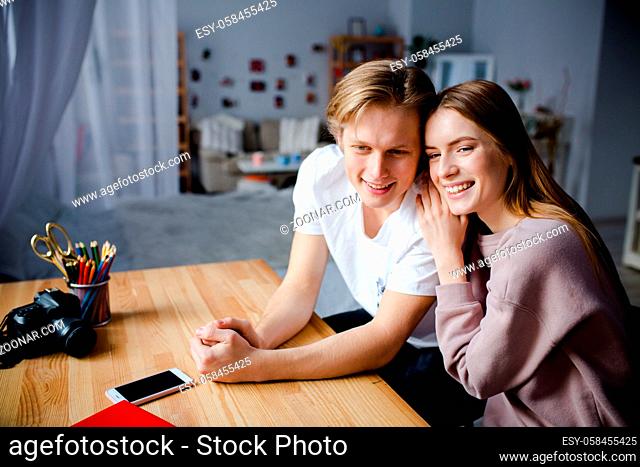Two stylish people happily spend time together. They are sitting at the table and discussing some plans