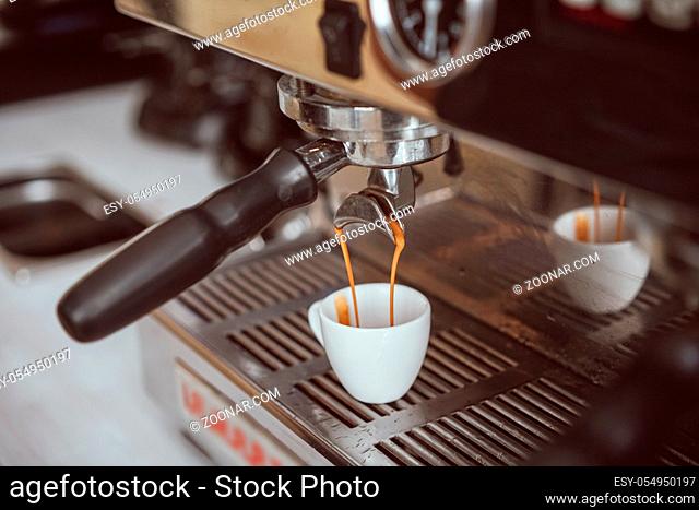 Professional espresso machine pouring fresh coffee into white ceramic cup with reflection on background