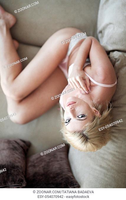 Portrait of a beautiful and sexy young blonde woman in white lingerie on couch, top view