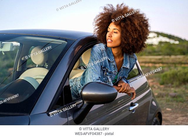 Young woman during road trip, leaning out of window