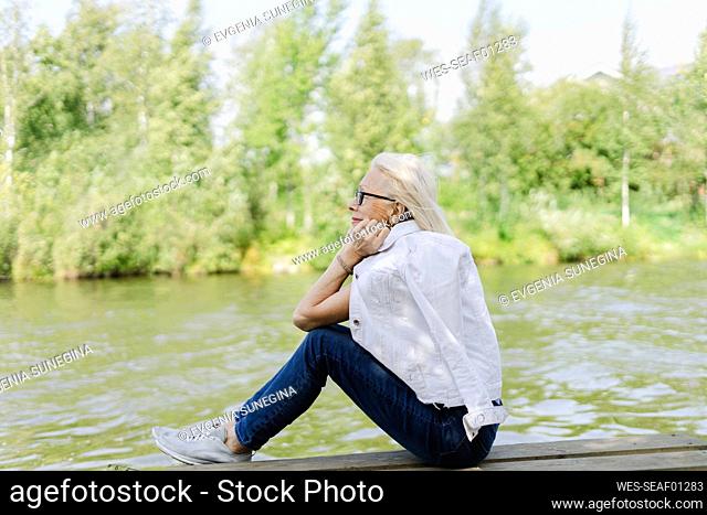 Senior woman day dreaming sitting on jetty near lake