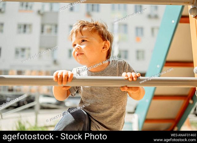Curious boy holding pole and climbing in playground