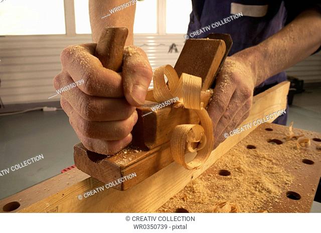 carpenter planing a plank, hands covered by sawdust