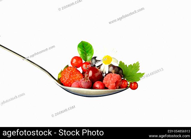 Large spoon of juicy forest berries of red currant, cherry, raspberry, black currant, with green leaves and chamomile flower on isolated background