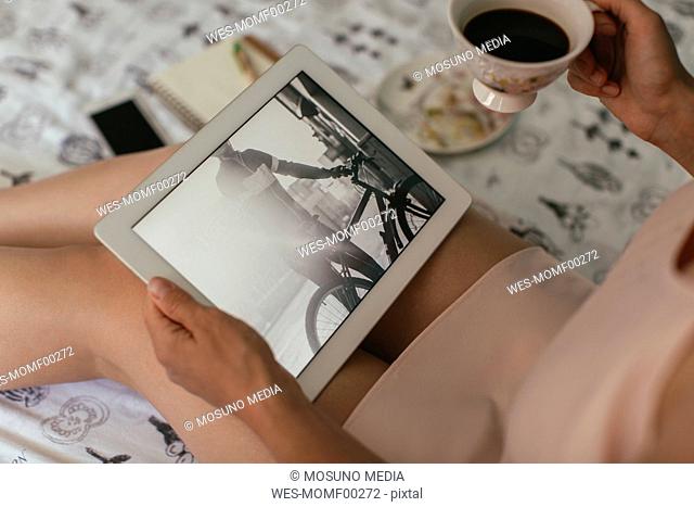 Woman sitting on bed loooking at photos on tablet