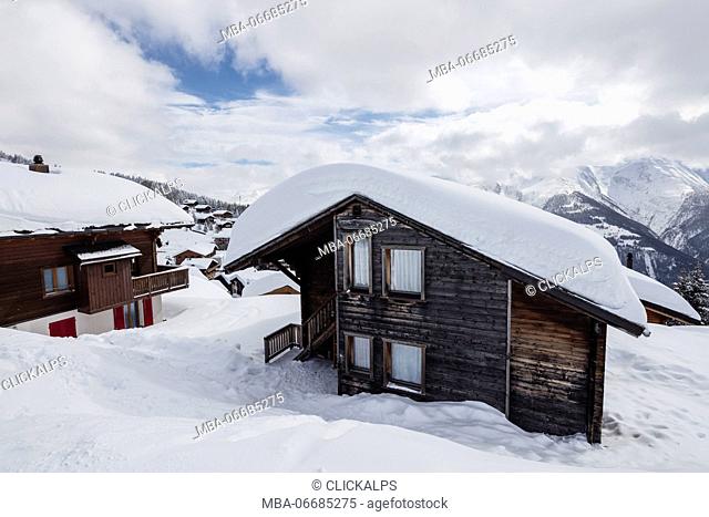 Clouds and blue sky frame the mountain huts covered with snow Bettmeralp district of Raron canton of Valais Switzerland Europe