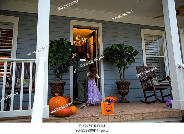 Brother and sister trick or treating at neighbour's front door