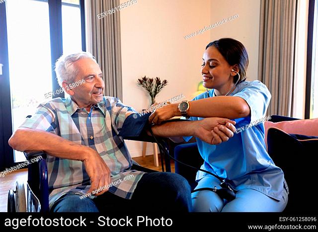 Biracial female doctor examining caucasian senior man's blood pressure with stethoscope and gauge