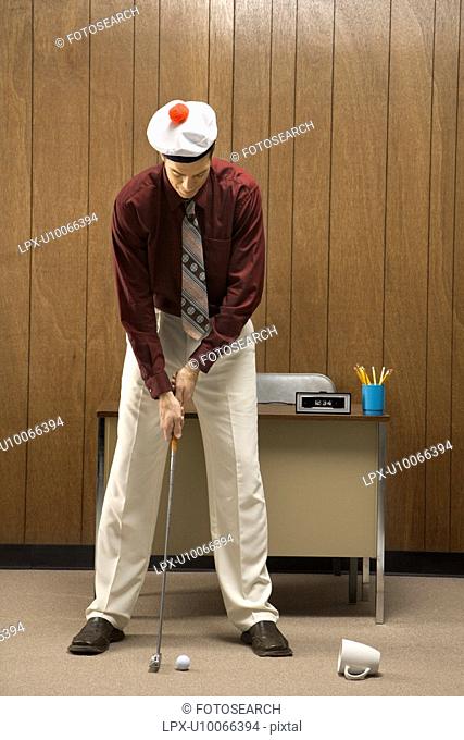 Caucasian mid-adult retro businessman wearing cap putting golf ball into coffee cup in his office