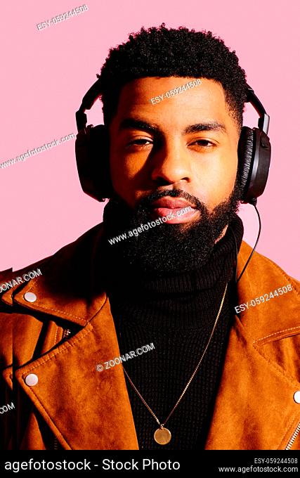 Portrait of a cool man with beard and headphones isolated on pink studio background