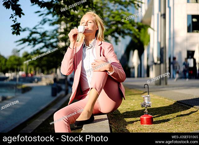 Female professional smelling coffee while sitting on camping stove in city during sunny day