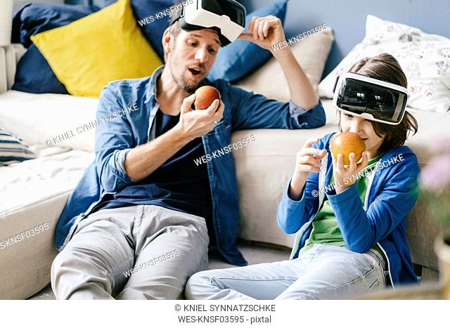 Father and son wearing VR glasses and eating apples at home