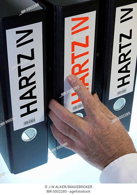 Hand reaching for a ring binder labeled Hartz IV, German term for long-term unemployment benefits, symbolic image
