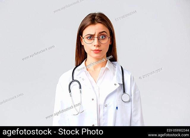 Healthcare workers, medicine, insurance and covid-19 pandemic concept. Skeptical and confused female doctor in white scrubs, medical suit and glasses
