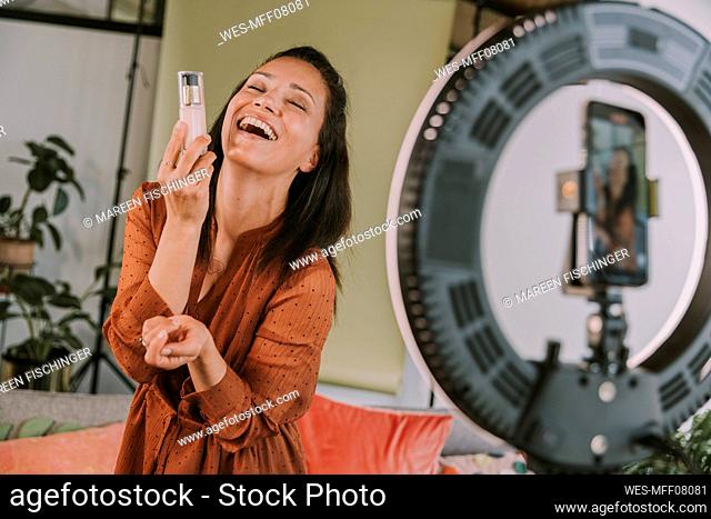 Laughing female influencer holding foundation while vlogging at home