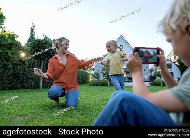 Boy photographing mother dancing with girl through mobile phone in garden
