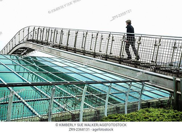 Man ascends a metal bridge over a glass roof at the Warsaw University Library garden, designed by Irena Bajerska and opened in 2002, Politechnika Warszawska