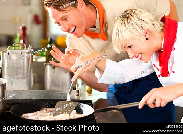 Two chefs in teamwork - man and woman - in a restaurant or hotel kitchen cooking delicious fish in pan