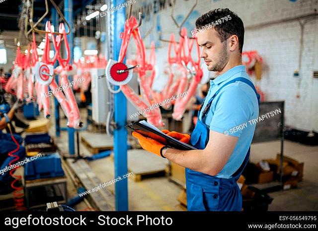 Bicycle factory, man with notebook checks bike assembly line. Male mechanic in uniform installs cycle parts in workshop, industrial manufacturing