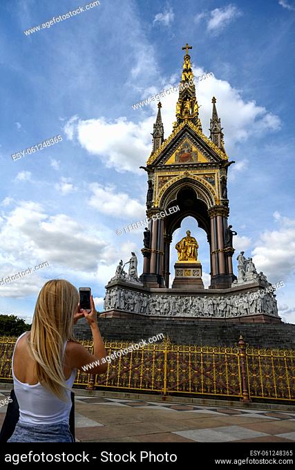 Female tourist taking photos of the exterior of the Royal Albert Hall from The Albert Memorial, Kensington, London, United Kingdom