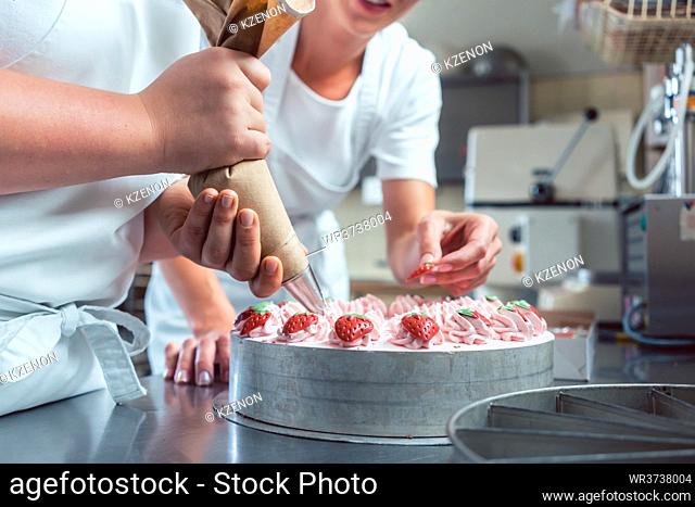 Confectioner or pastry chefs finishing cake with pastry bag, close-up on hands