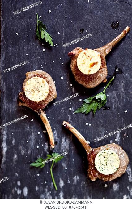 Three differently flavoured compound butters on lamb chops and parsley leaves on slate