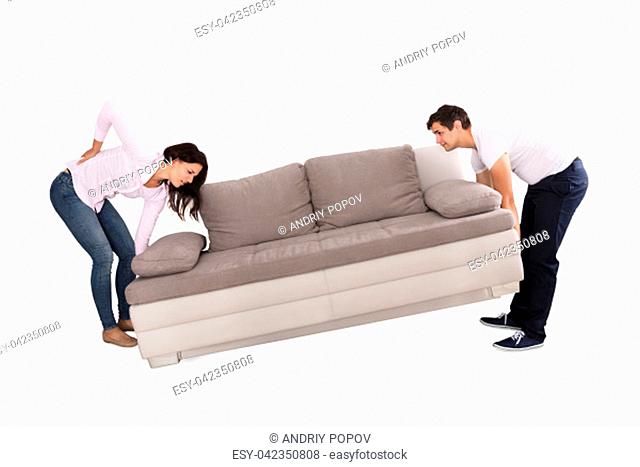 Young Woman Suffering From Back Pain While Lifting Sofa With Her Husband On White Background