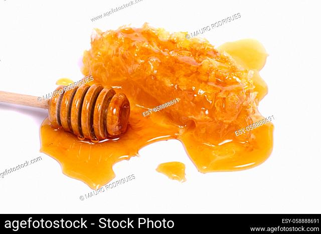 Natural honey spilled on a white background next to a honey dipper and honeycomb