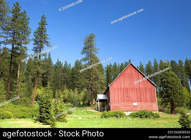 A red barn stands amongst green pine trees and a grassy field near Coeur d'Alene, Idaho