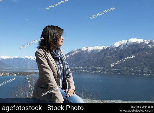 Woman Sitting and Enjoy the Panoramic View over Alpine Lake Maggiore with Snow-capped Mountain in Ascona, Switzerland