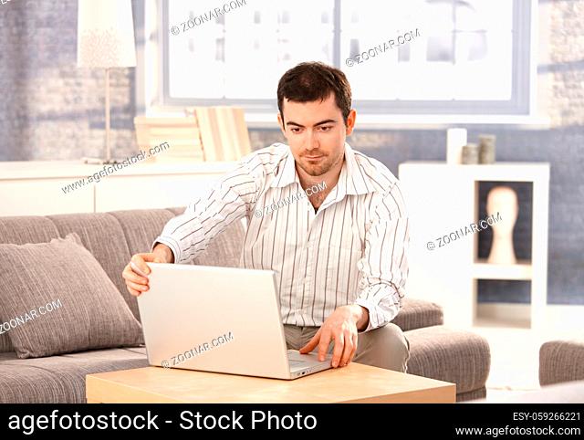 Young man browsing Internet at home, sitting on sofa, looking at screen