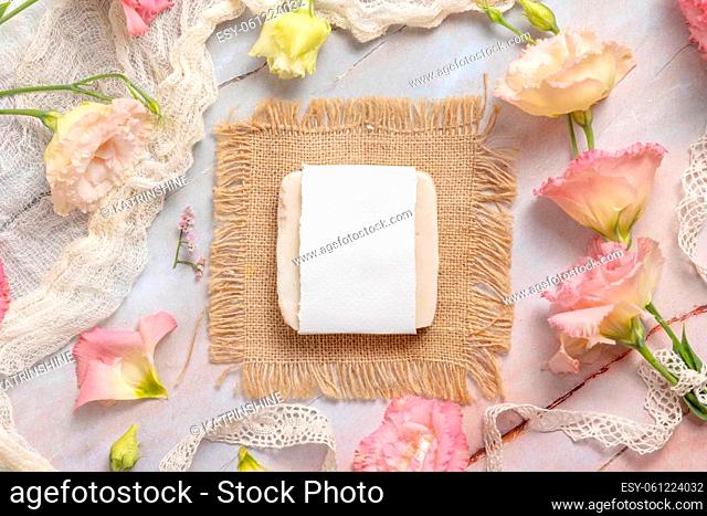 Soap bar on laying on a marble table with pink flowers, petals and vintage ribbons, top view. Soap mockup