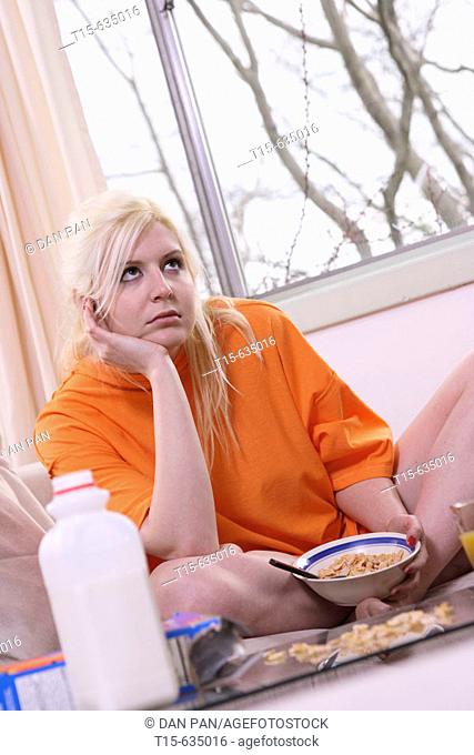 Young woman staring at ceiling while eating cereal