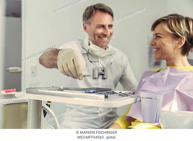 Dentist putting instruments on tray after treatment, looking at his smiling patient