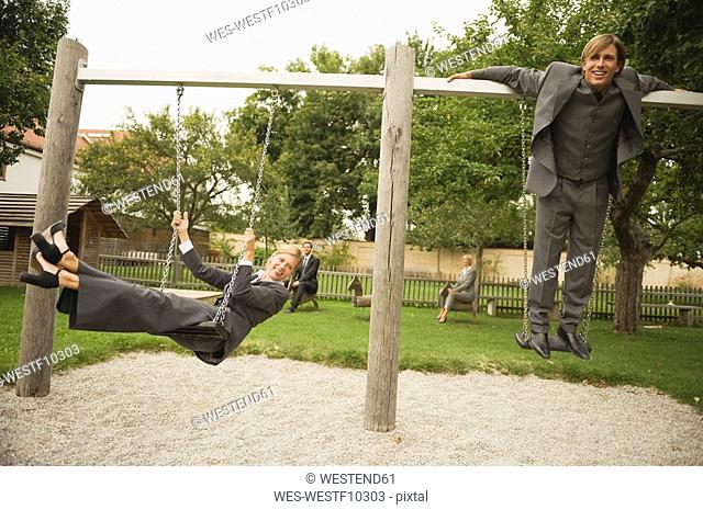 Germany, business people sitting on swings in playground